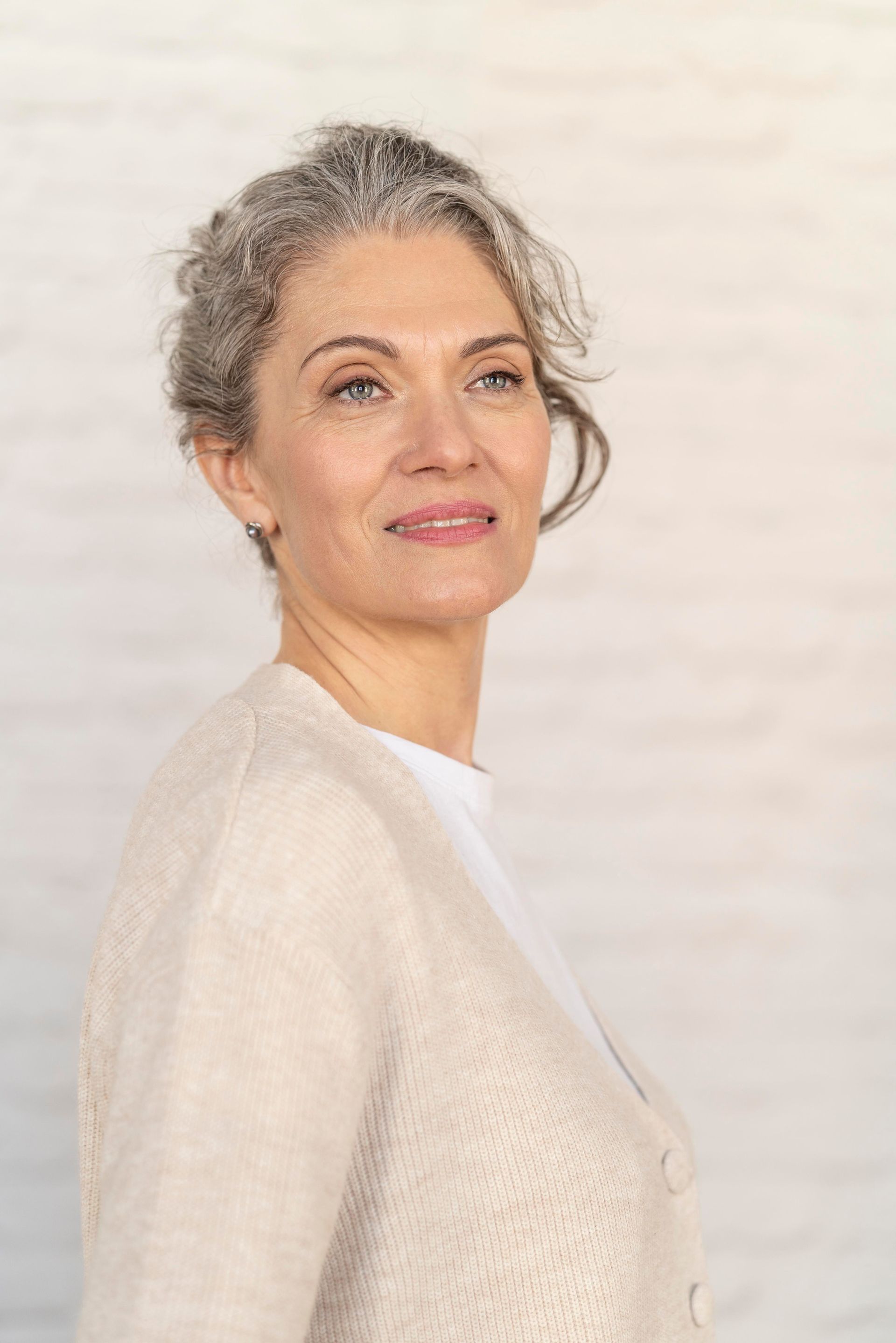 A woman with gray hair is standing in front of a white wall.