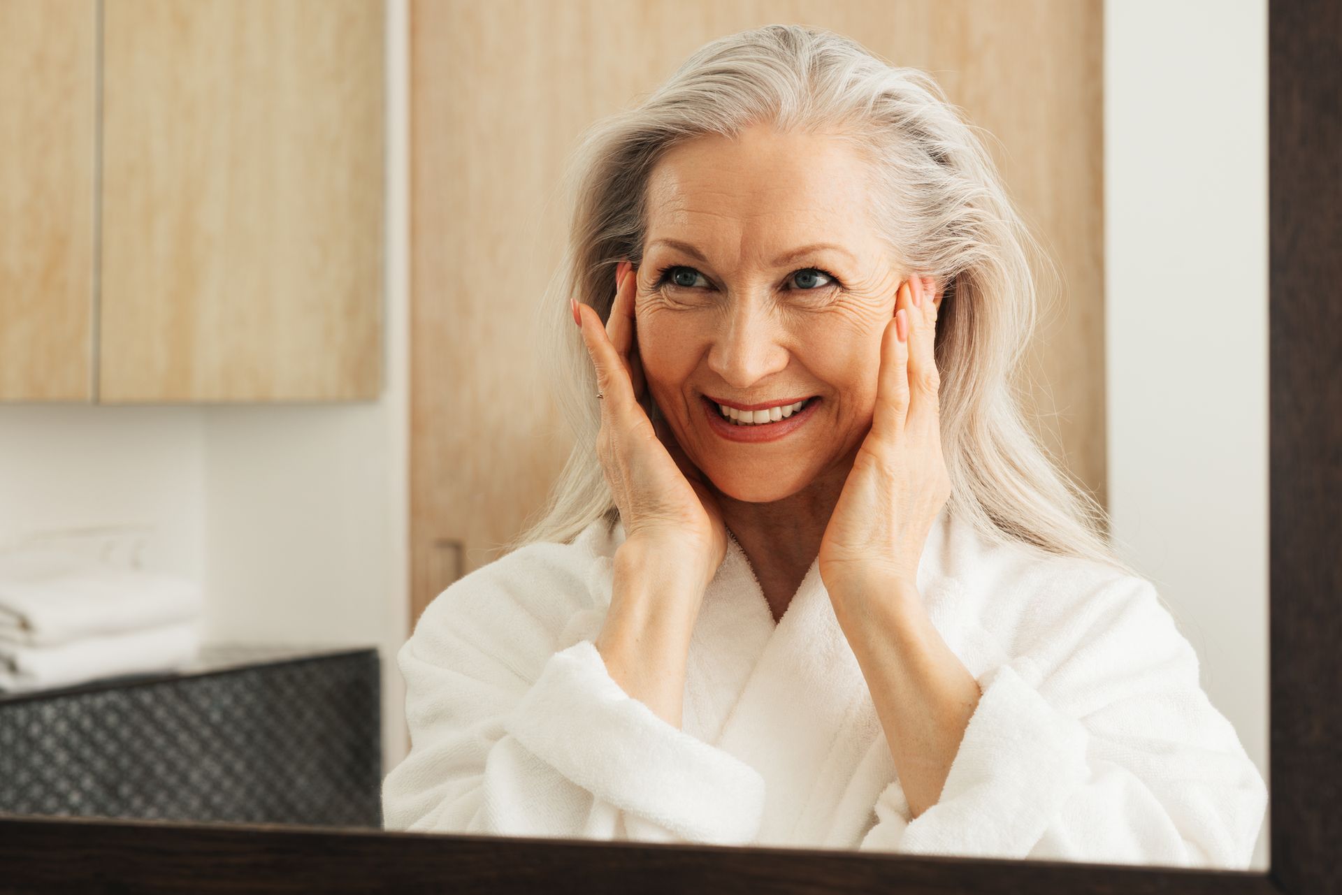 An older woman is looking at her face in a bathroom mirror.