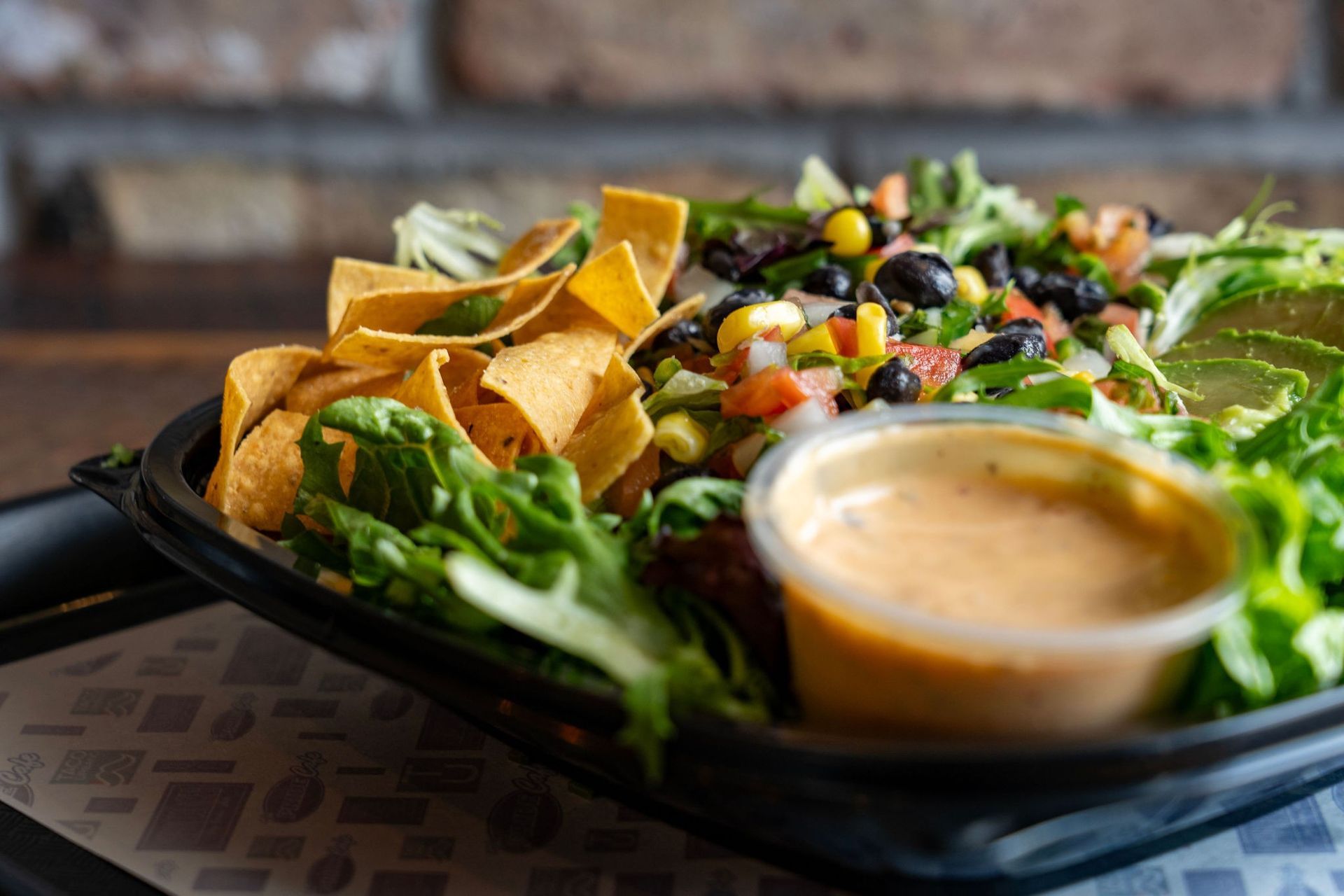 Salad with tortilla chips, black beans, corn, salsa, avocado, and dressing in a black container.