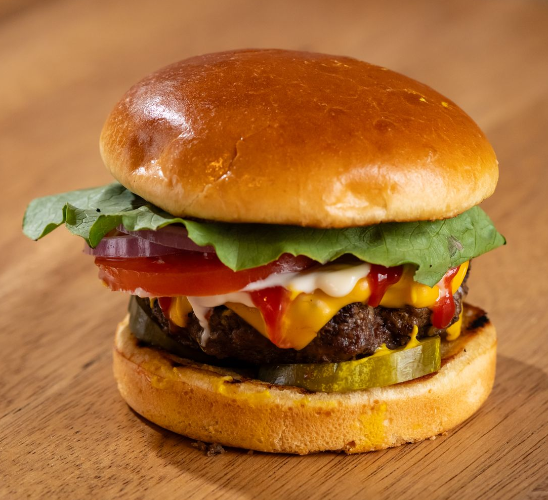 Cheeseburger on a bun with lettuce, tomato, red onion, and pickles on a patterned tray.