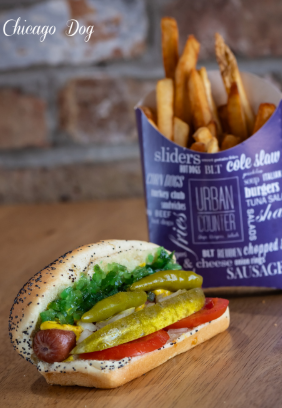 Chicago-style hot dog with toppings, next to a container of fries. Brick background.