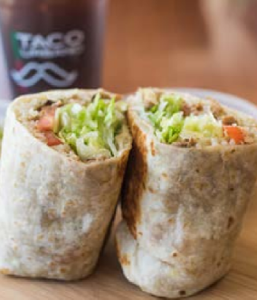 Burrito cut in half, filled with lettuce, tomato, and meat, with a drink in the background.