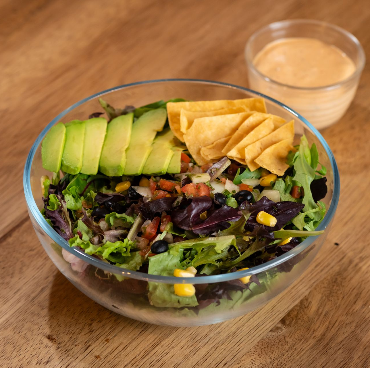 Salad with avocado, corn, black beans, chips, and dressing.