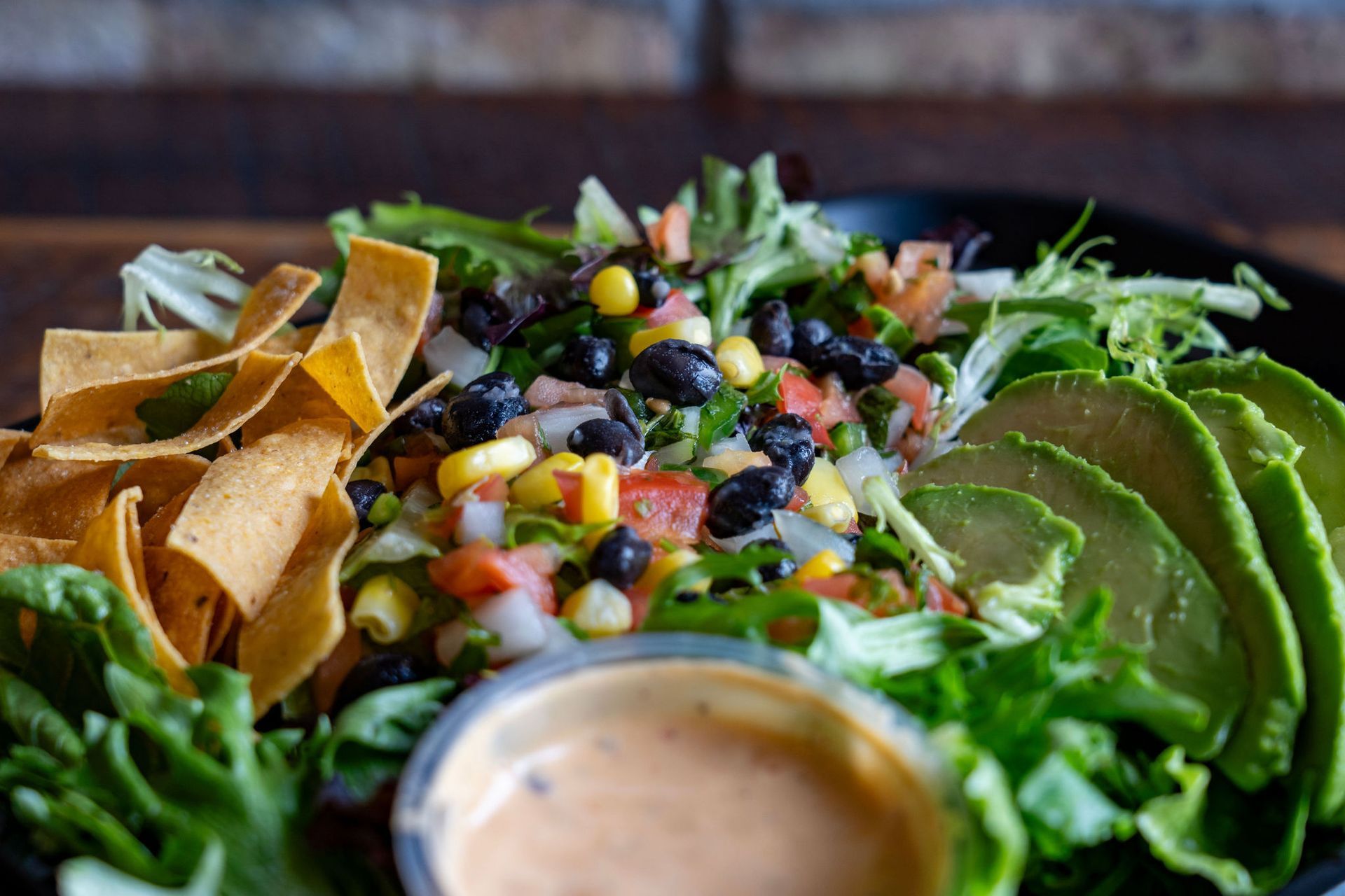 Salad with lettuce, avocado, corn, beans, salsa, and tortilla chips; dipping sauce in a cup.