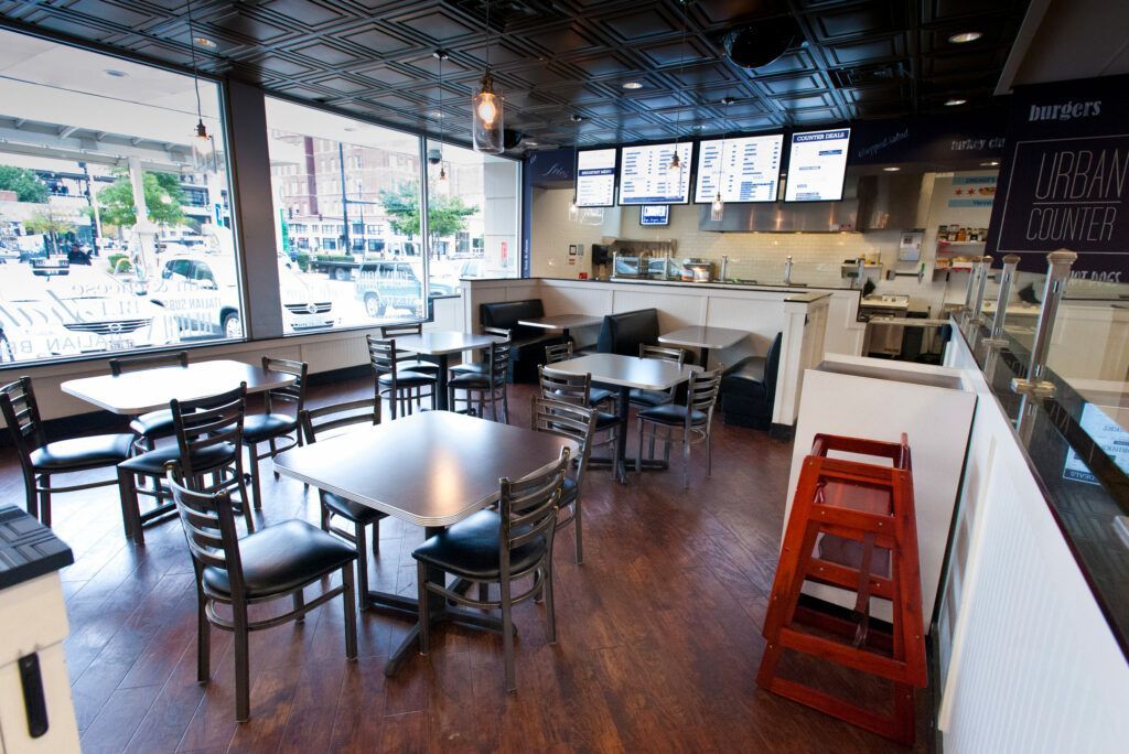 Restaurant interior with tables, chairs, and a high chair; large windows offer an outside view.
