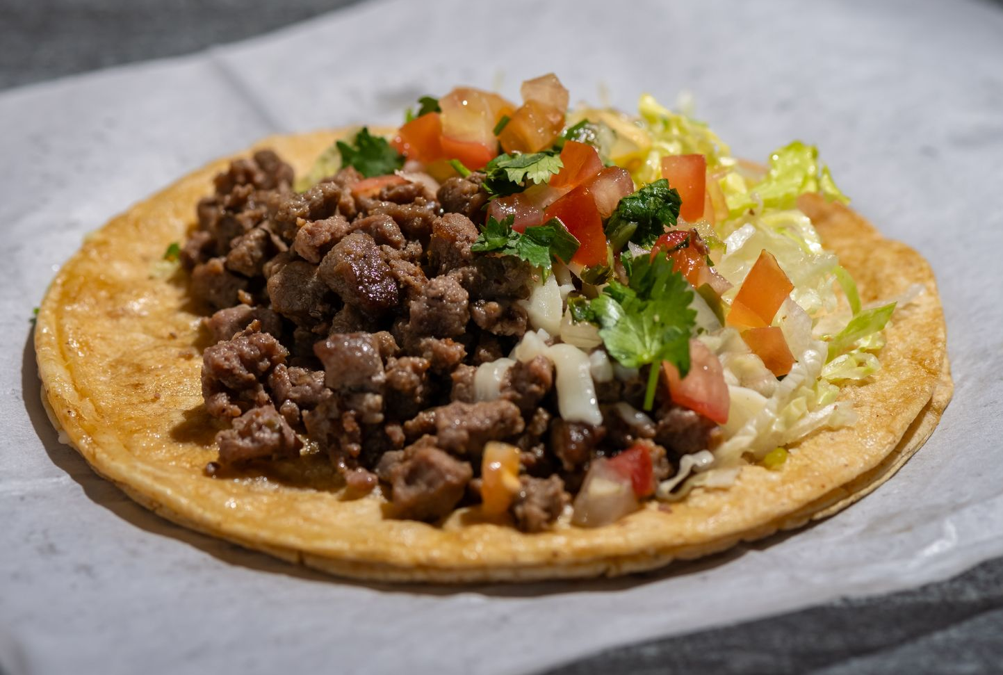 Burrito cut in half, filled with lettuce, tomato, and meat, with a drink in the background.