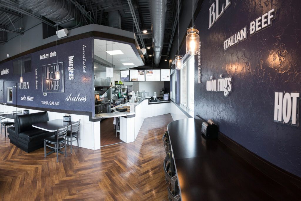 Interior of a restaurant with dark blue walls, wooden floors, a counter, and a menu board.