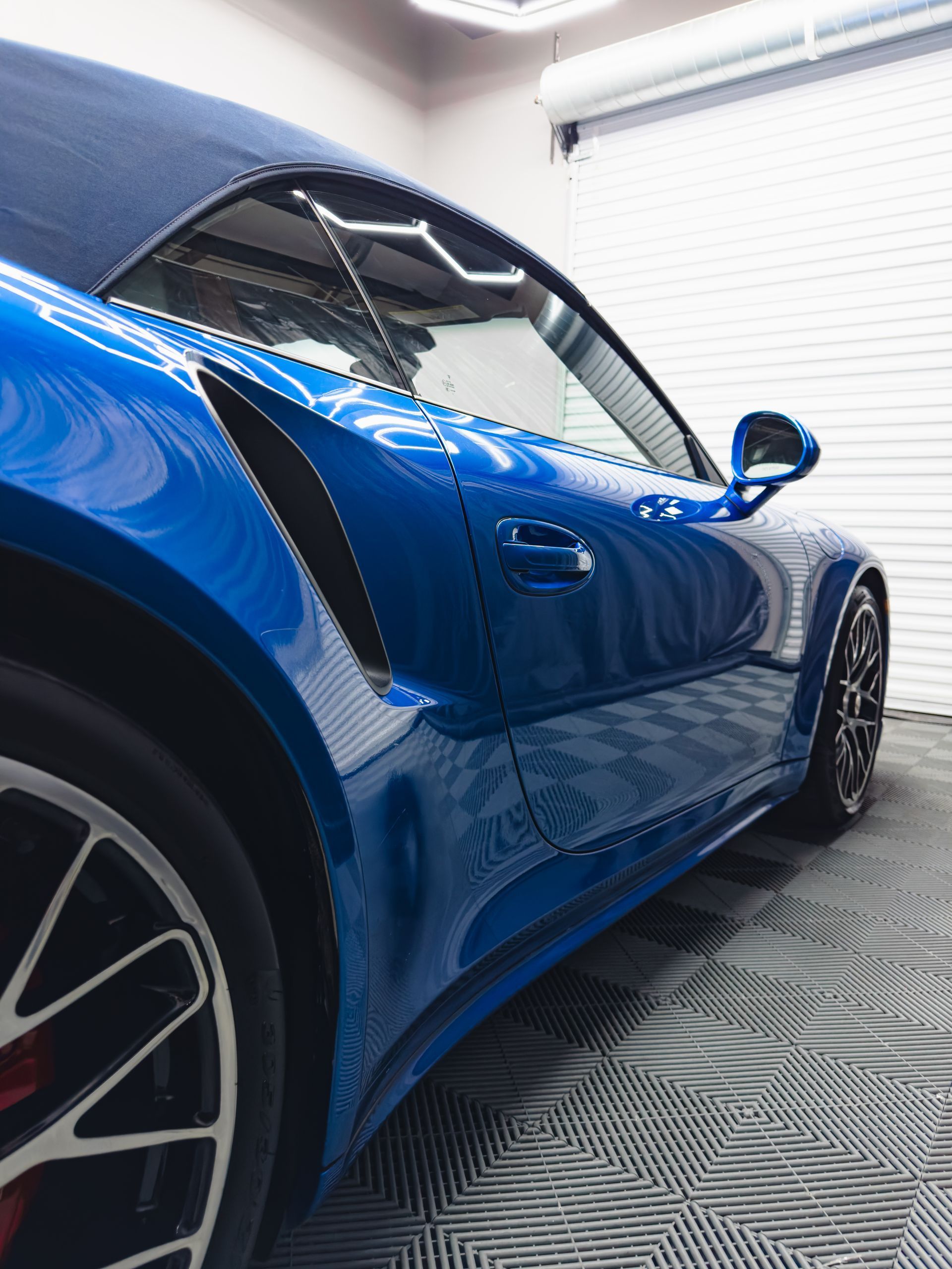 Blue sports car fender, reflecting light, with a polishing tool in the lower right.