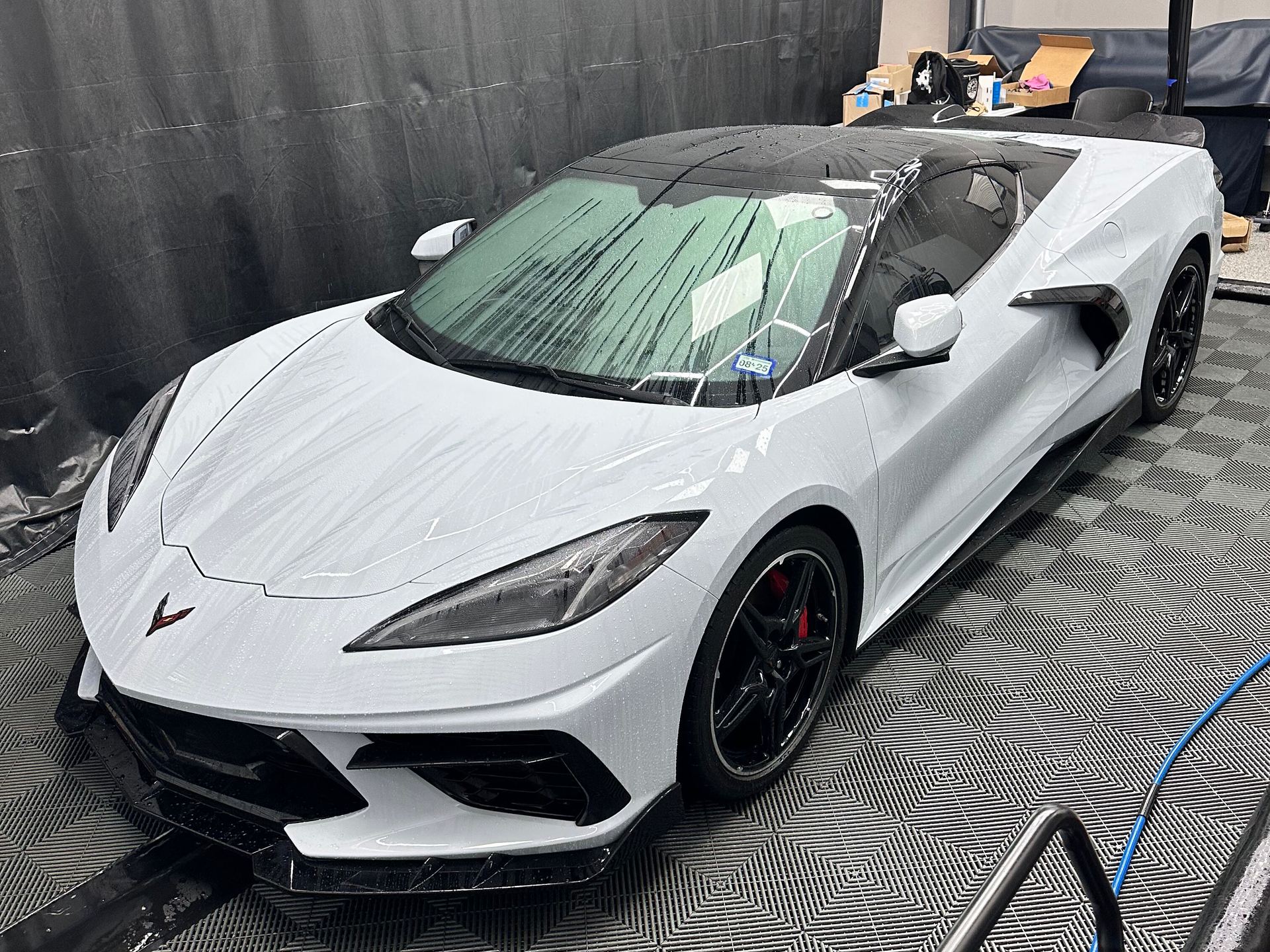 White Corvette with black trim and wheels in a garage, possibly being washed.