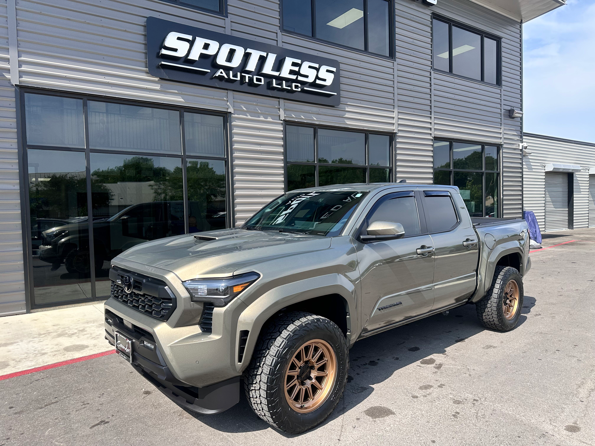 A tan Toyota Tacoma truck parked in front of Spotless Auto LLC, a car dealership.