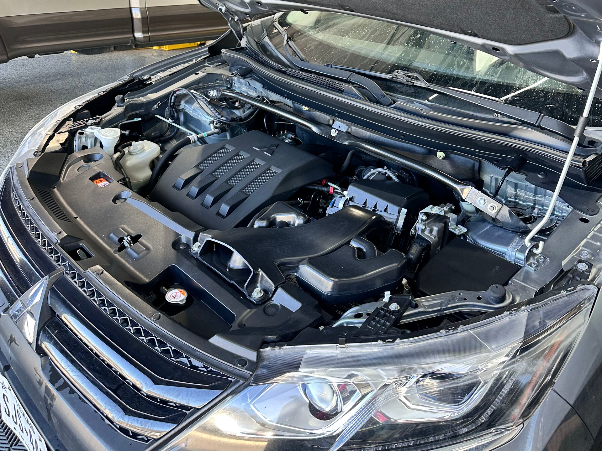 A car engine compartment, showing the engine and various components, with the hood open.