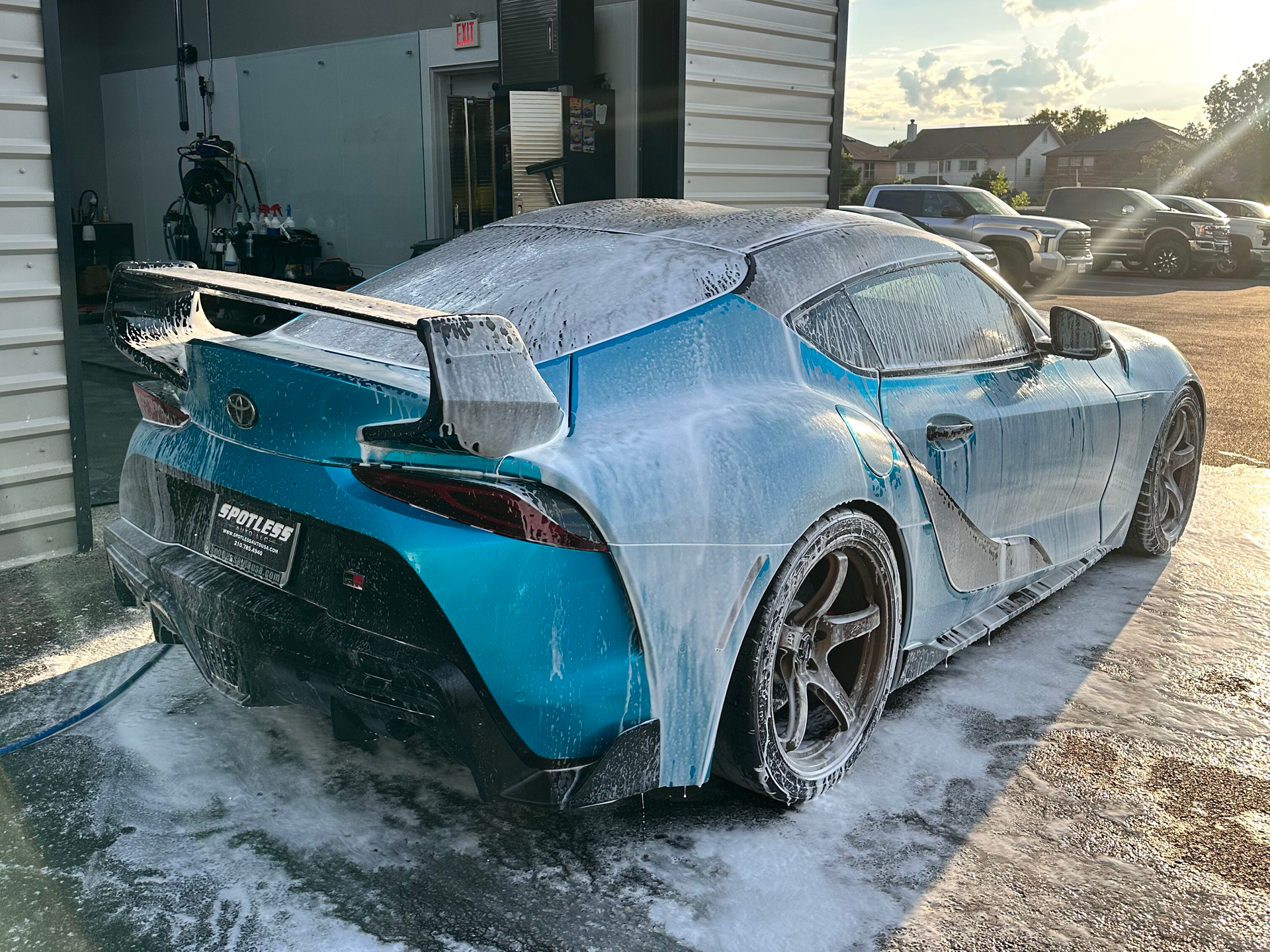 Blue Toyota Supra covered in soap suds during a car wash, outdoors.