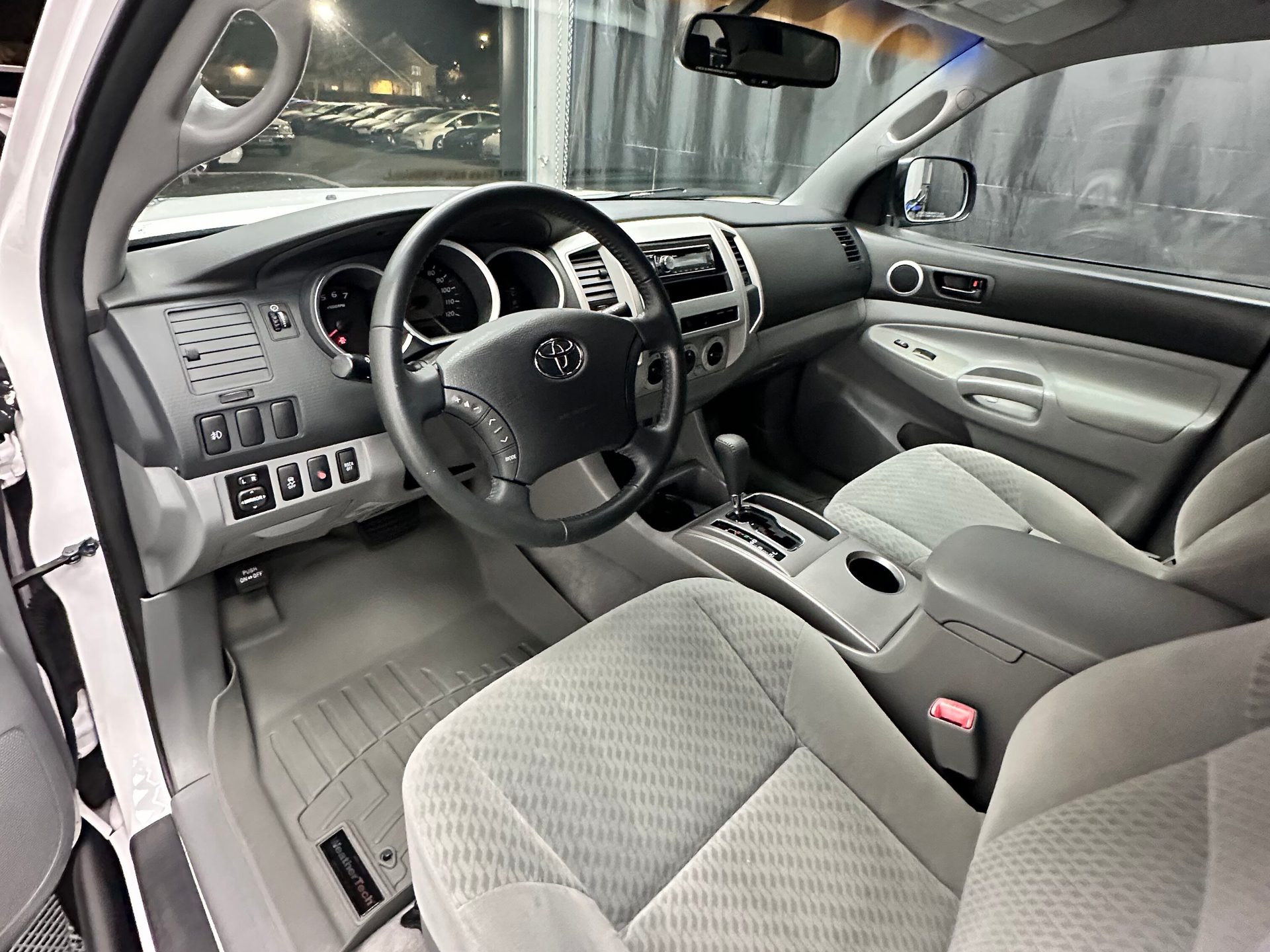Interior of a light-colored Toyota Tacoma, showing the dashboard, steering wheel, and seats.