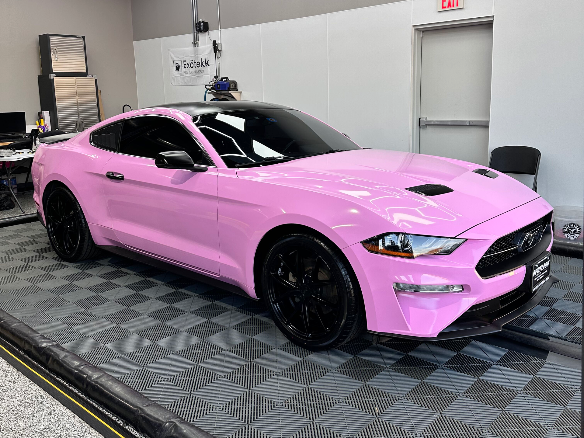 Pink Ford Mustang coupe with black wheels parked indoors.