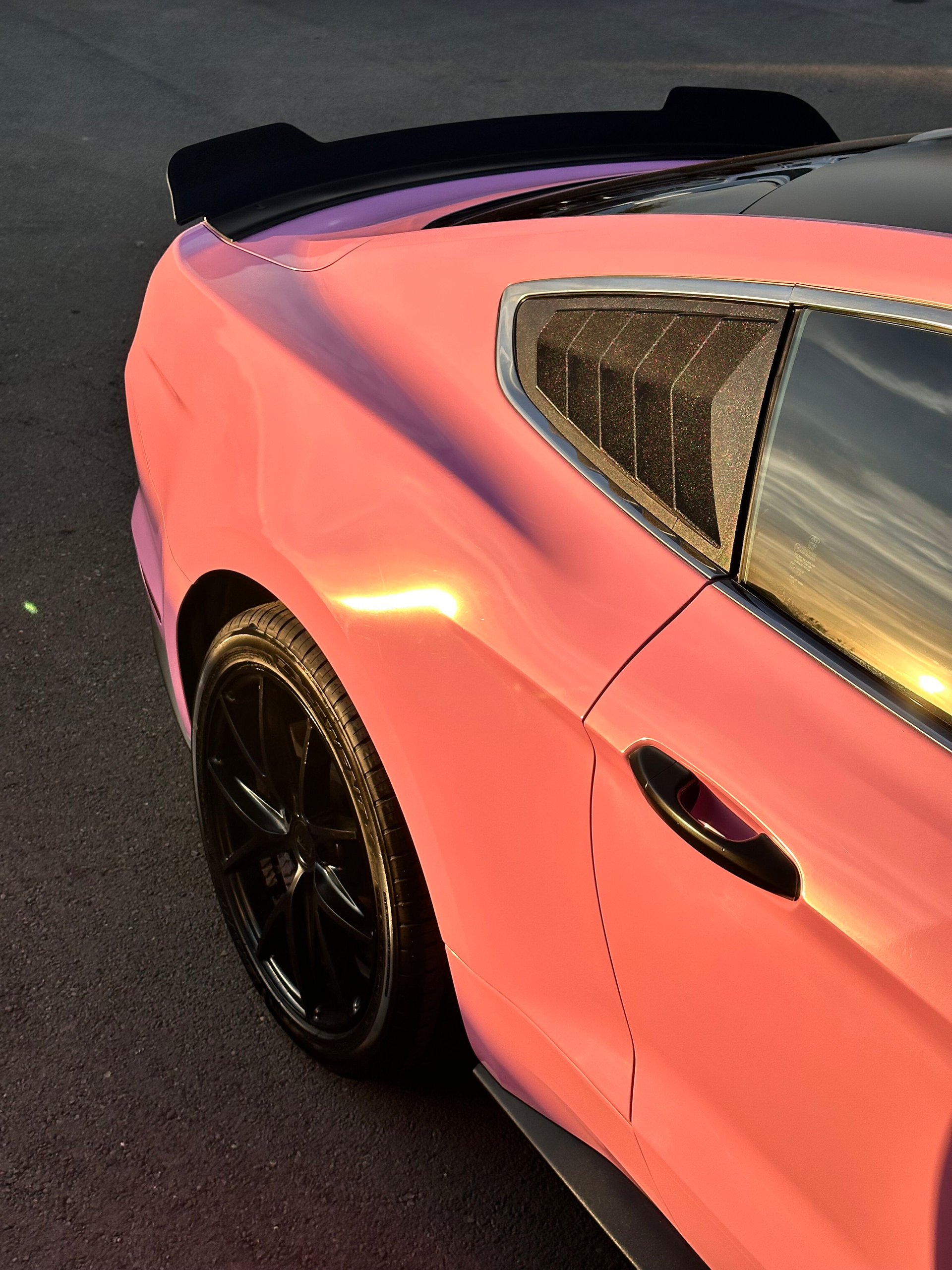 Pink Ford Mustang with black accents, including wheels and a spoiler. The car is parked outdoors.