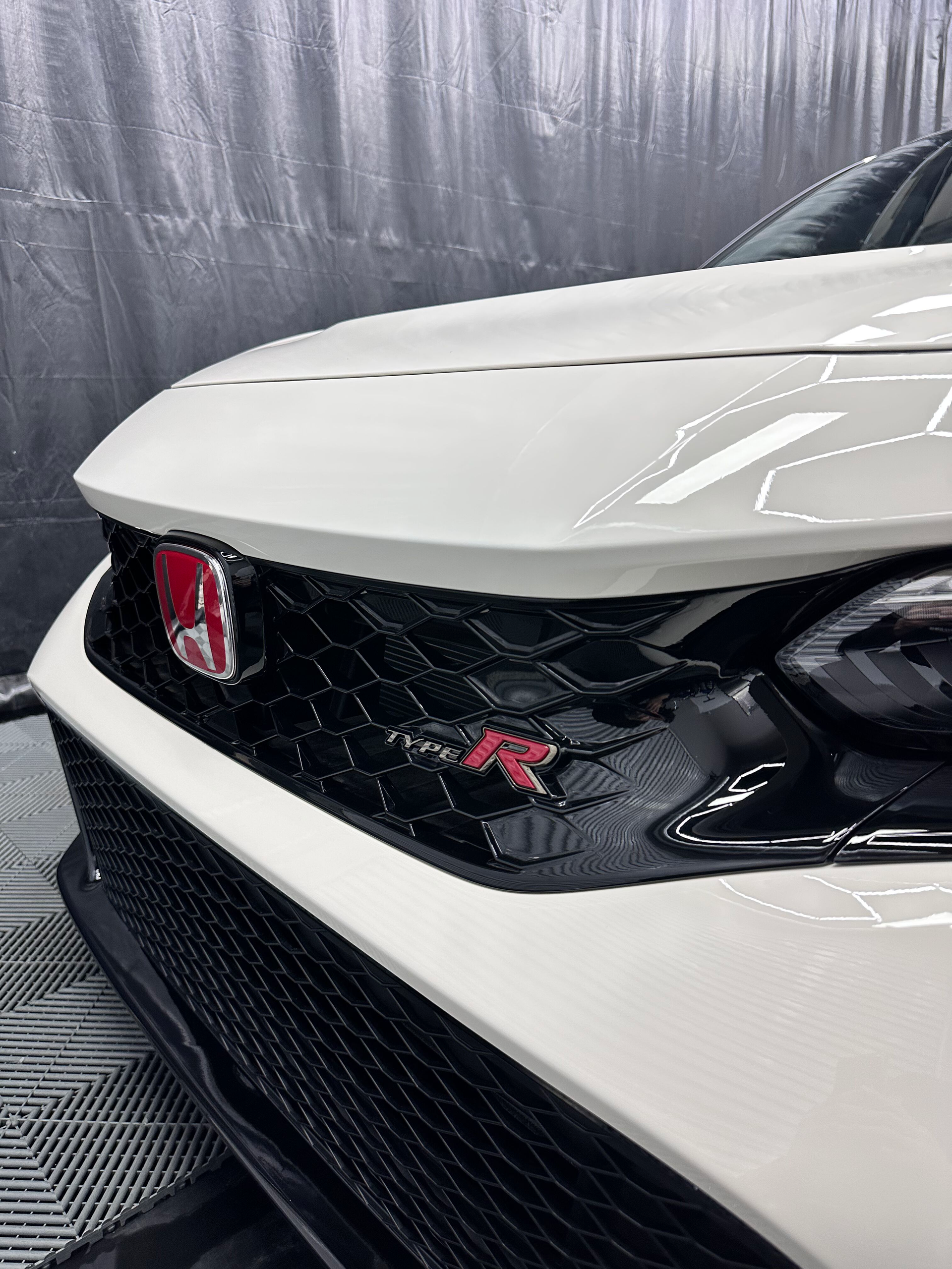 White Honda Civic Type R car front, red badges, black grille, in a garage.