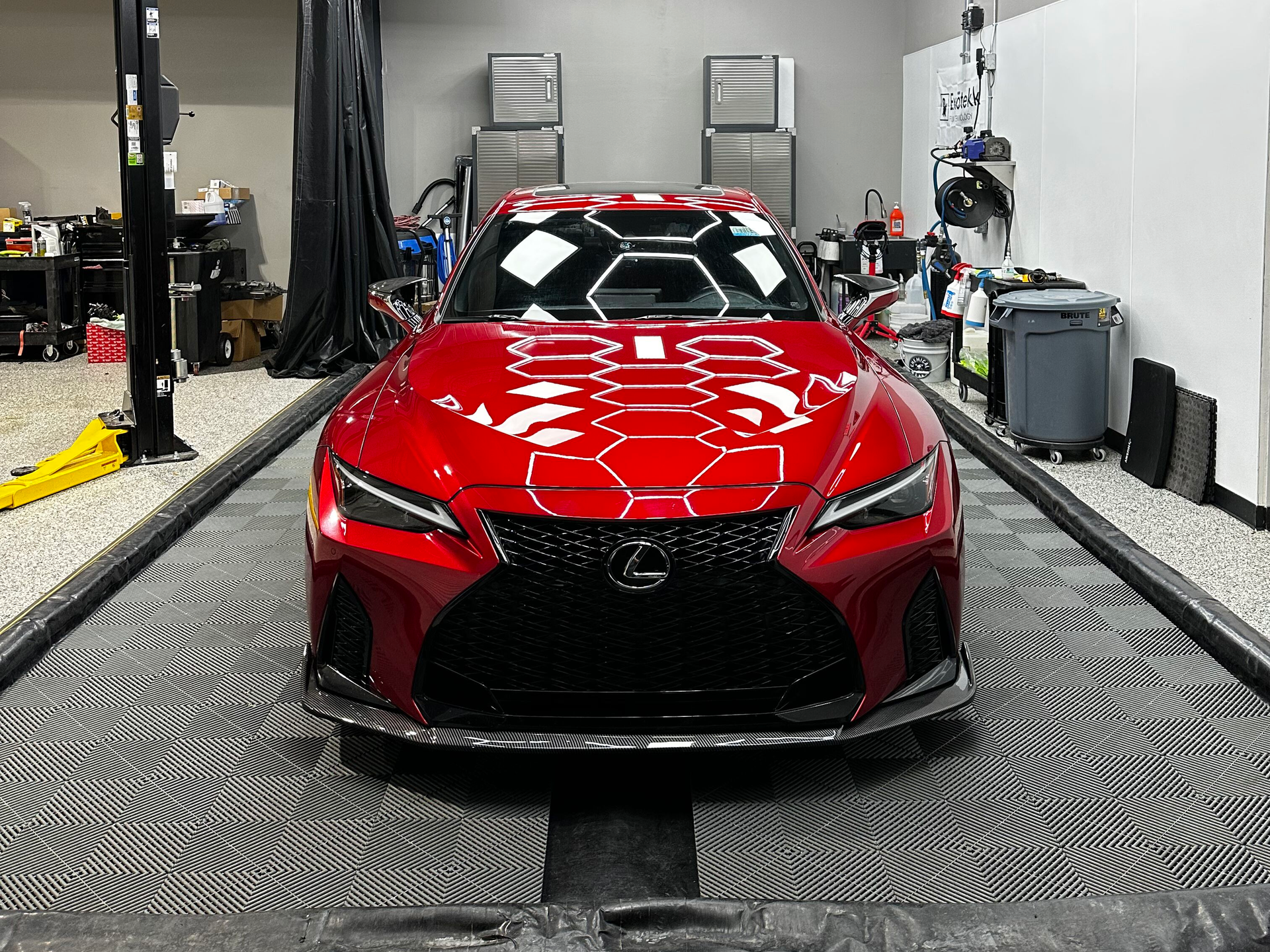 Red Lexus sports car on a garage floor, with a black grill and hexagonal patterned reflections on the hood.