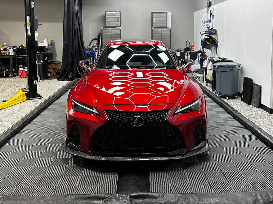 Red Lexus sports car centered on a garage platform. The car's hood reflects overhead lights.