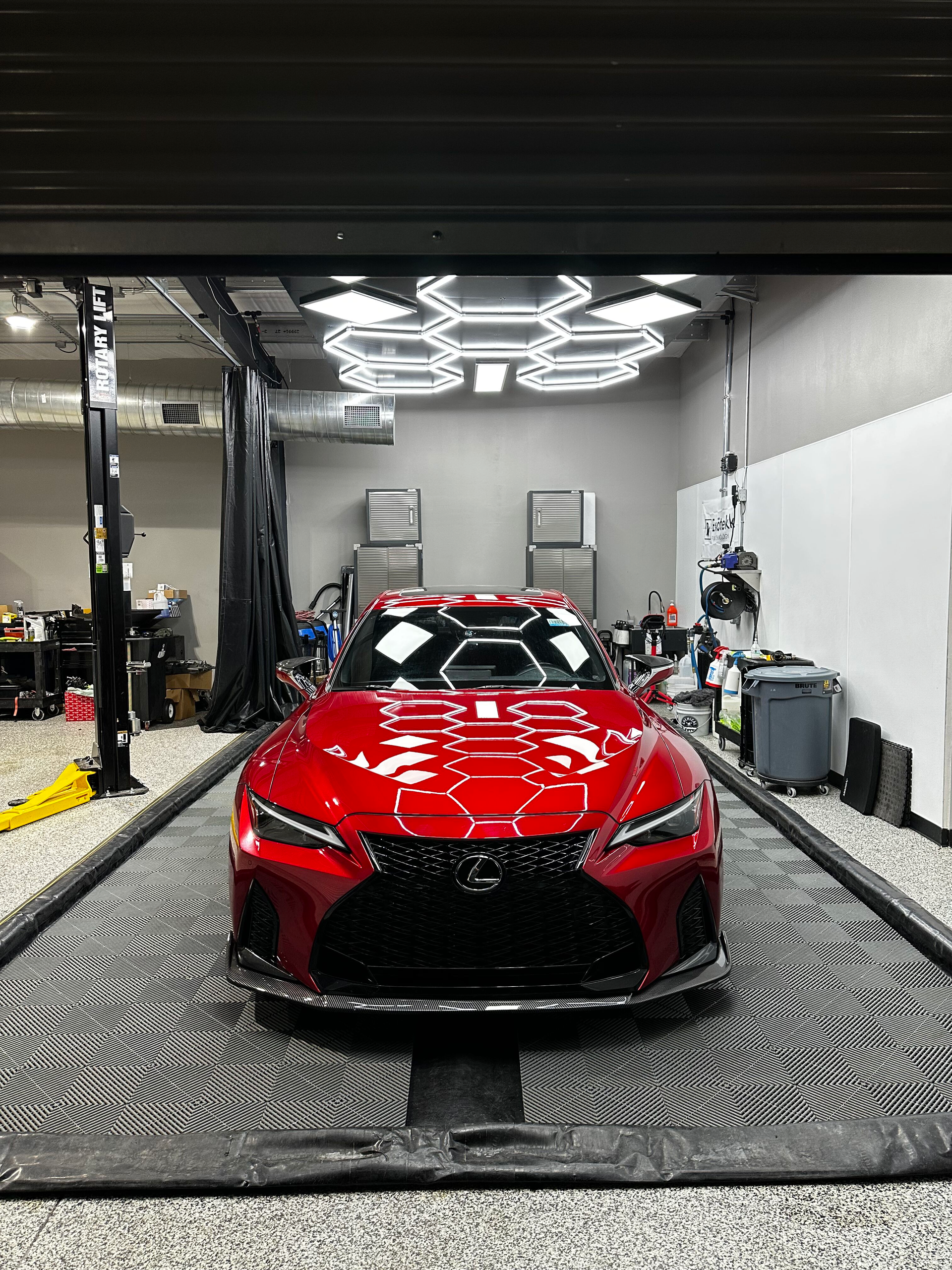 A shiny red Lexus sports car inside a well-lit garage, surrounded by detailing equipment.