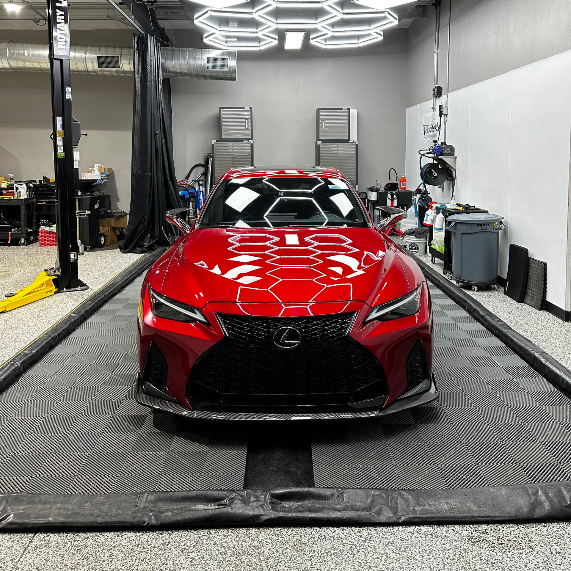 A red Lexus sports car is inside a car detailing shop, centered on a black mat.