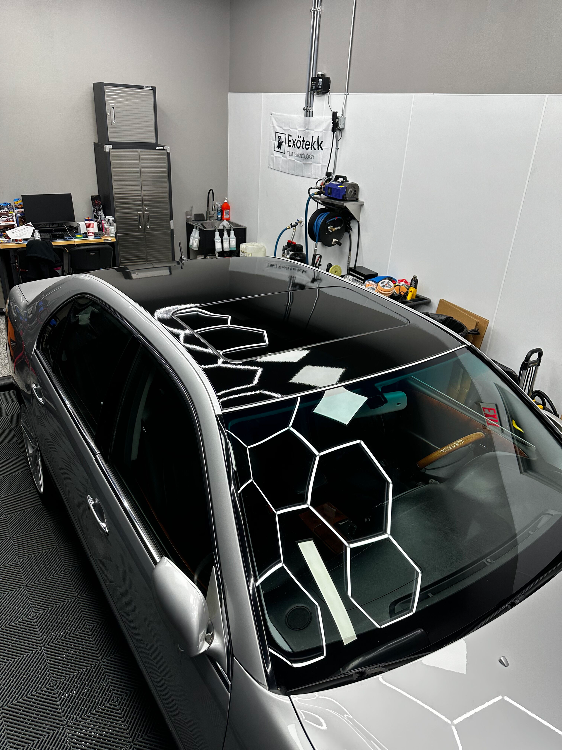 A gray car with a black roof and hexagon-patterned masking, inside a car detailing garage.