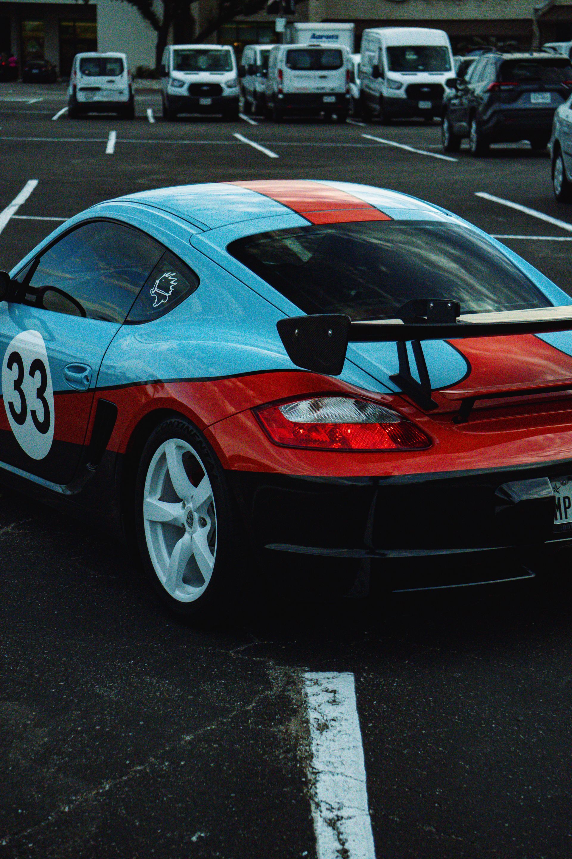 Red Corvette car, close-up view. Showing front wheel, side vent, side mirror, and body panel in outdoor setting.