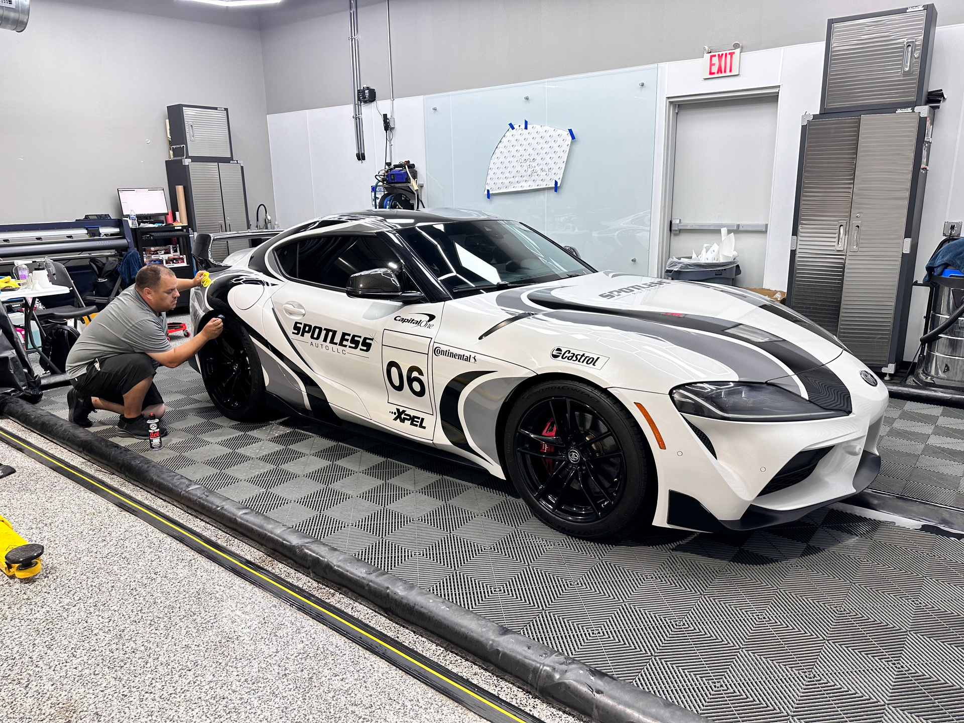 Man working on a white and black race car, likely applying vinyl in a garage setting.