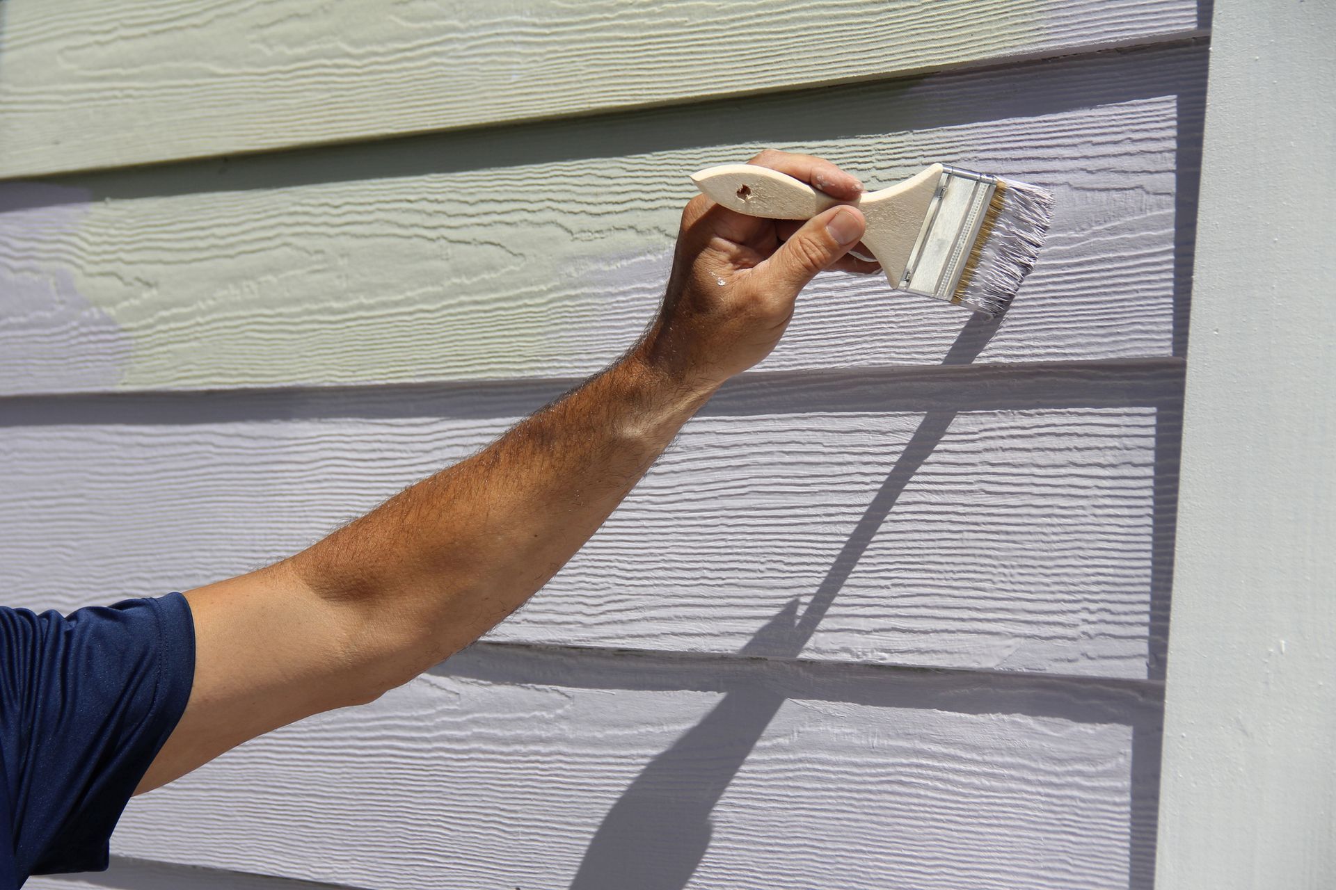 A man using a paintbrush to apply exterior paint to a house, showcasing home improvement efforts.