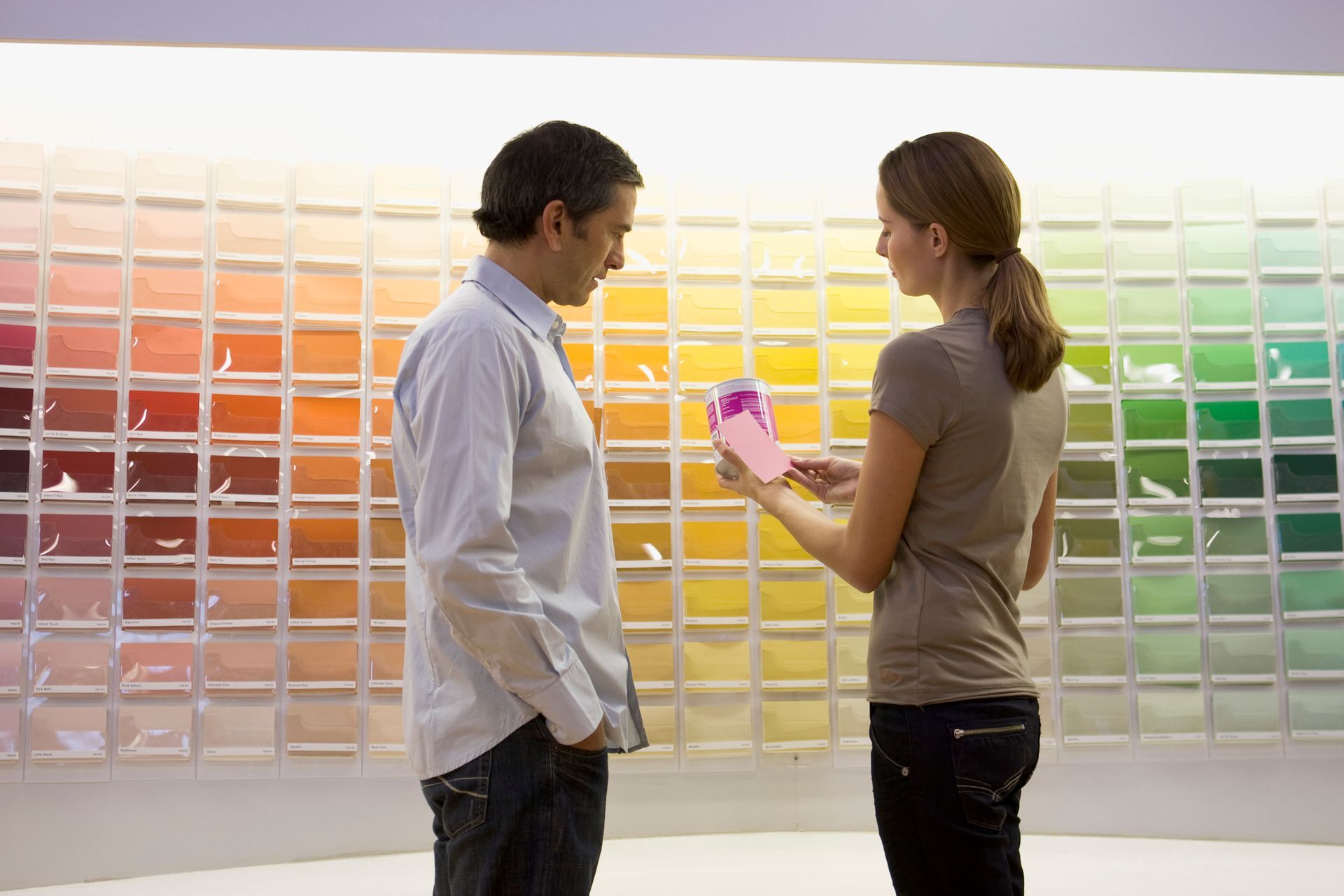 Two people choosing colors from a vibrant wall of paint samples.