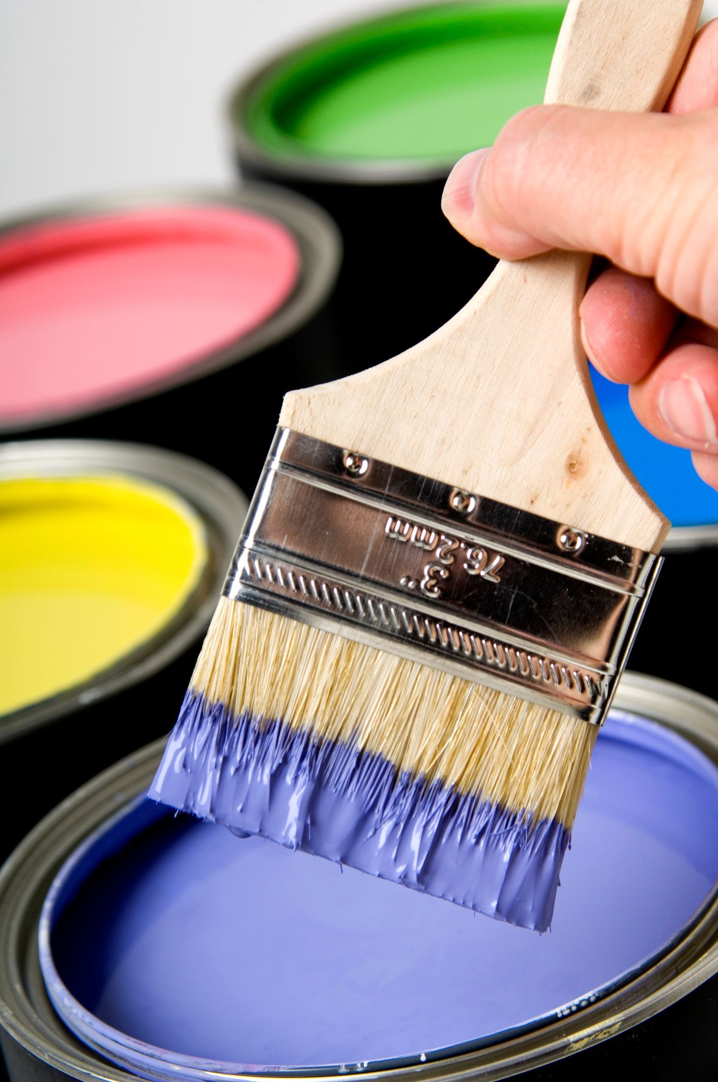 A person is holding a paint brush over a can of purple paint.