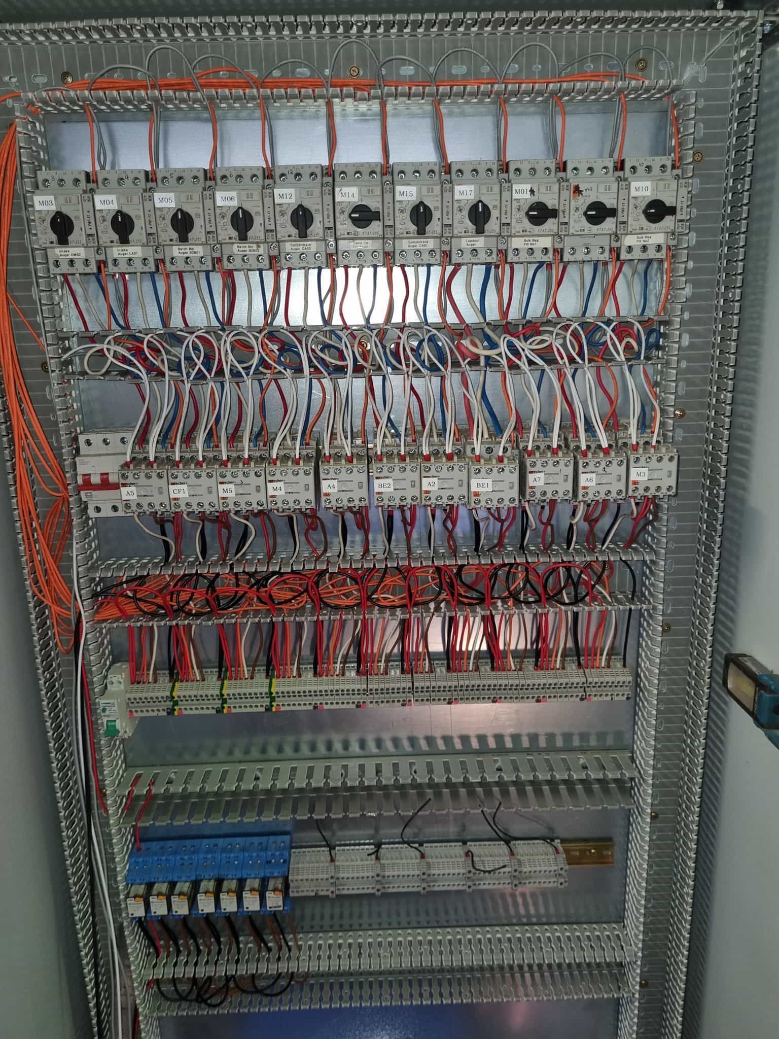 Control panel with numerous wires, circuit breakers, and switches. Metallic frame with organized wiring.