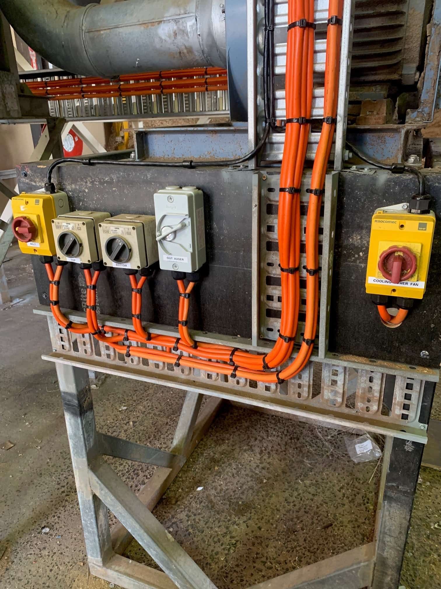 Electrical control panel with orange cables, switches, and conduit on a metal frame.