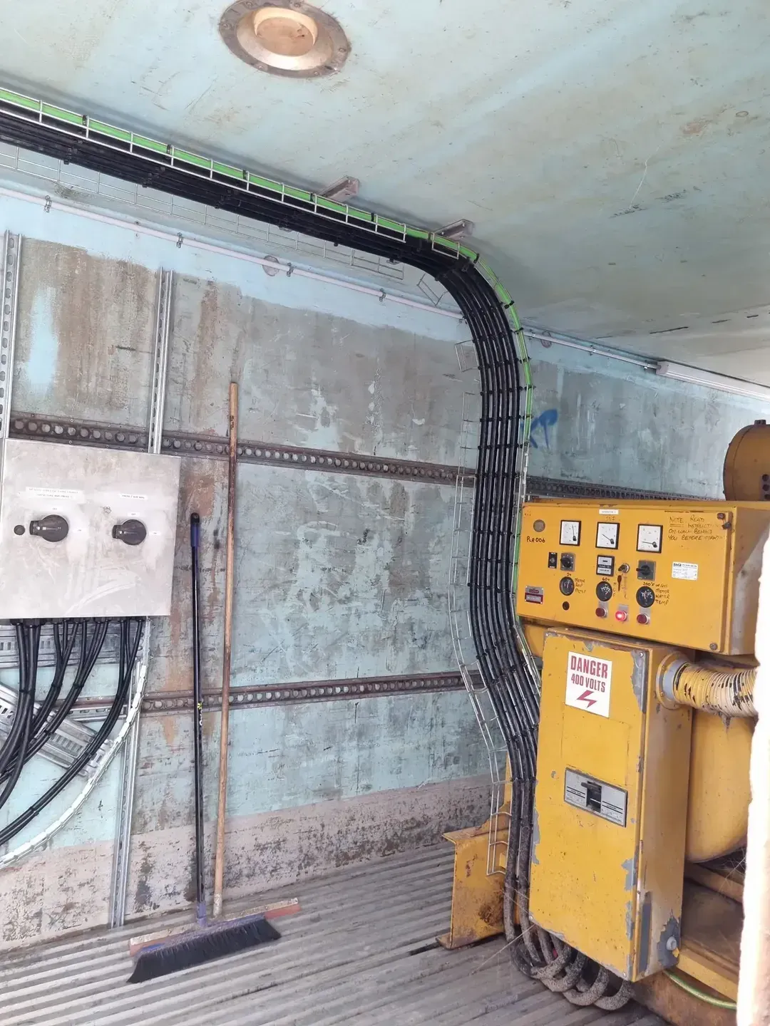 Interior of a room with electrical wiring along the walls and equipment. Wires are black, equipment yellow.