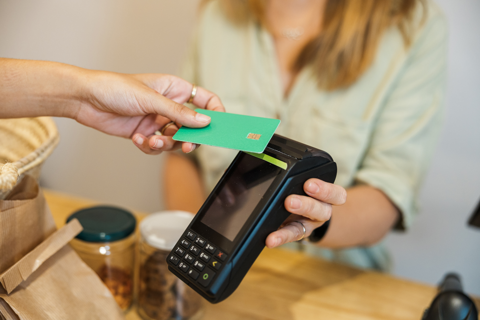 A person paying with a green contactless credit card on a handheld terminal at a counter.