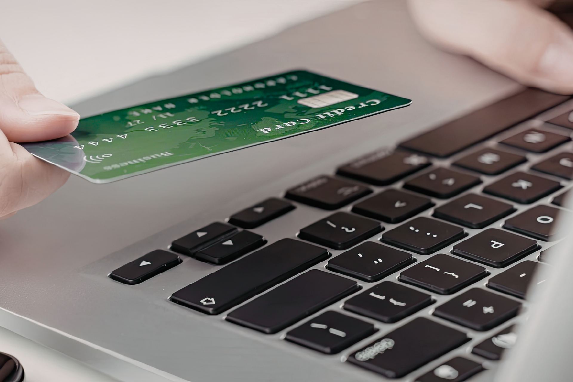 Hands holding a green credit card over a laptop keyboard, preparing to make an online purchase.