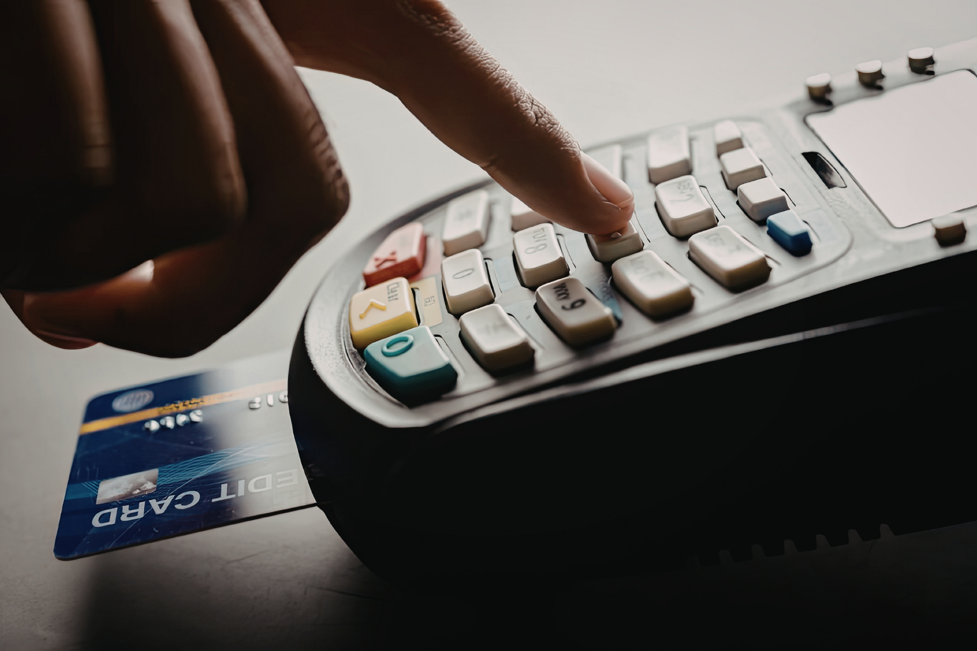 A hand inserting a blue credit card into a payment terminal and pressing a button to complete a transaction.
