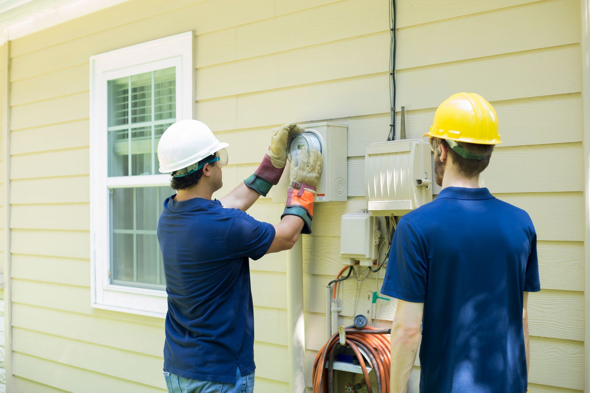 Two men are working on a meter on the side of a house.