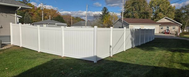 A white vinyl privacy fence encloses a green grassy backyard on a sunny day.