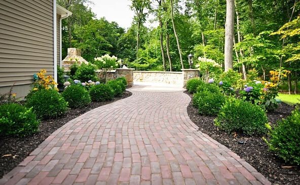 A brick walkway leading to a house surrounded by trees and bushes.