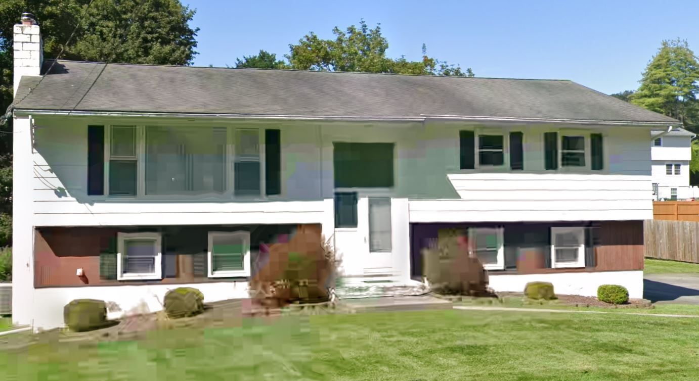 A large white house with a gray roof is sitting on top of a lush green lawn.