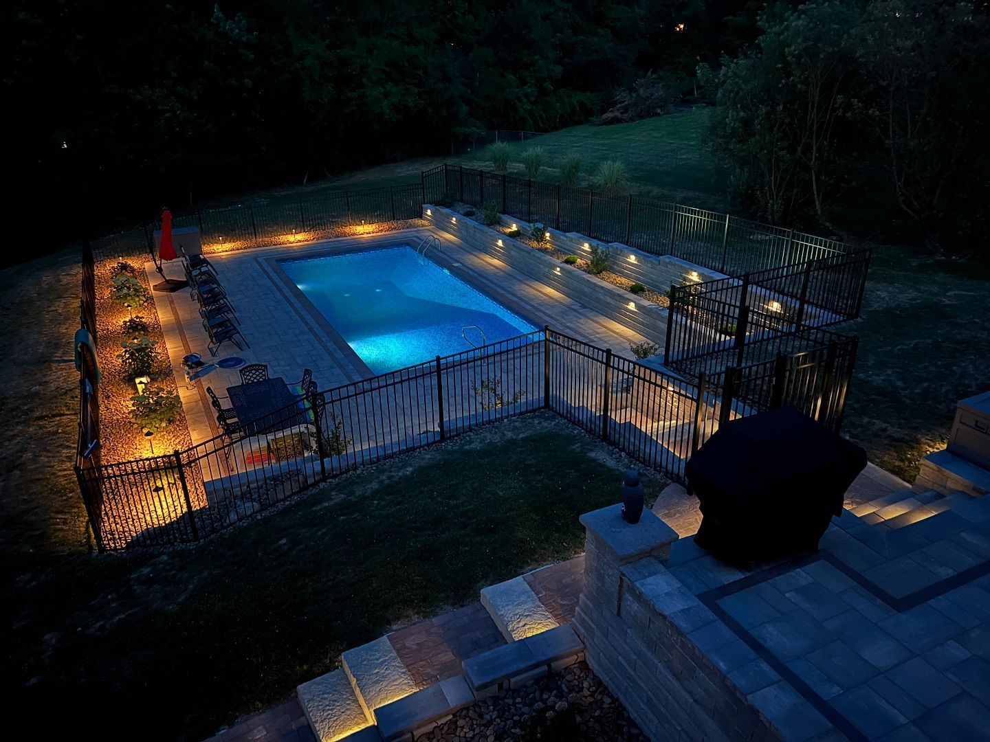 A large swimming pool is lit up at night in a backyard.