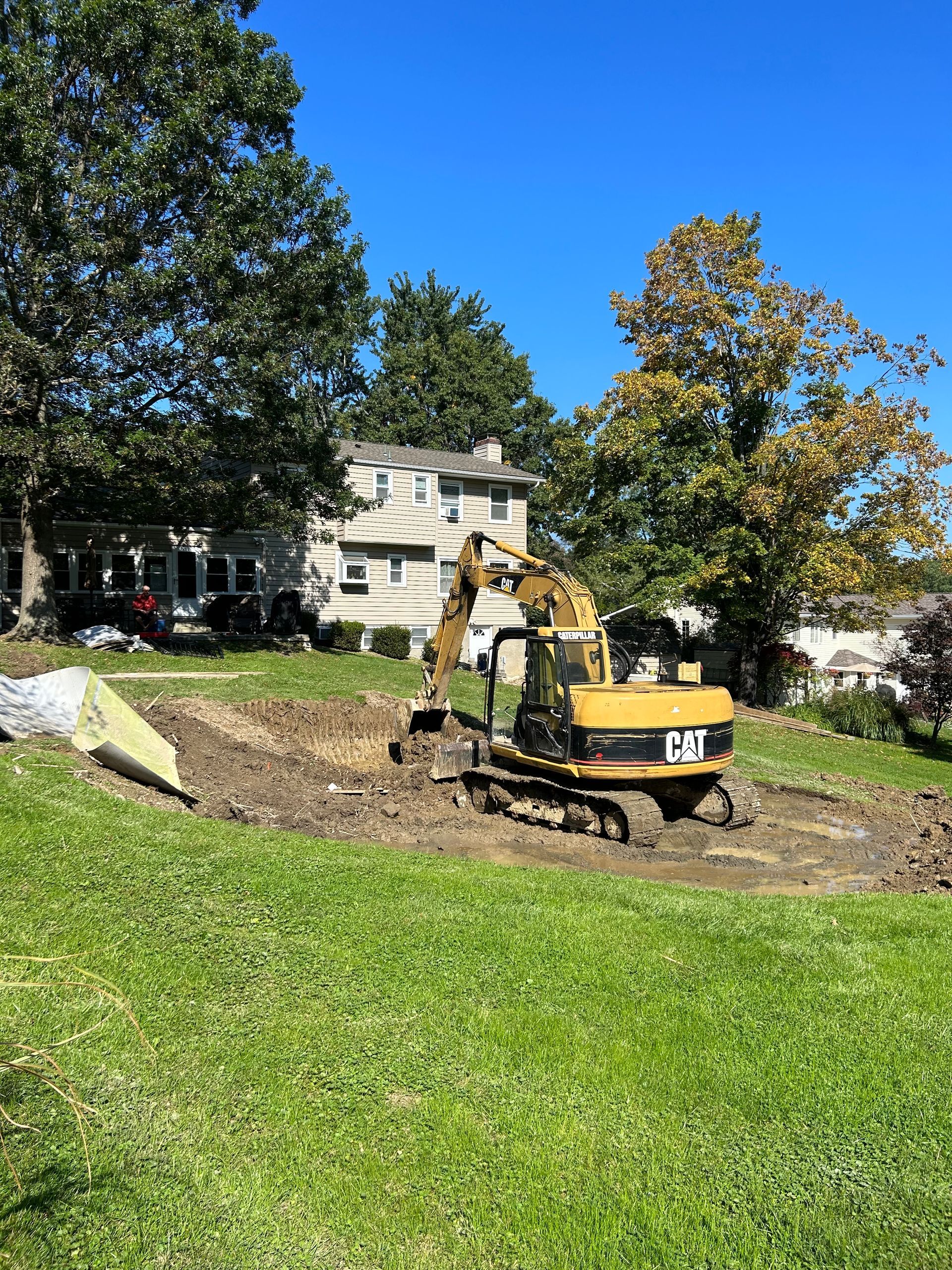 A cat excavator is digging a hole in the grass