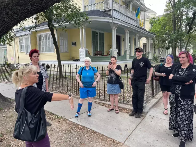 A group of people are standing on a sidewalk in front of a house.