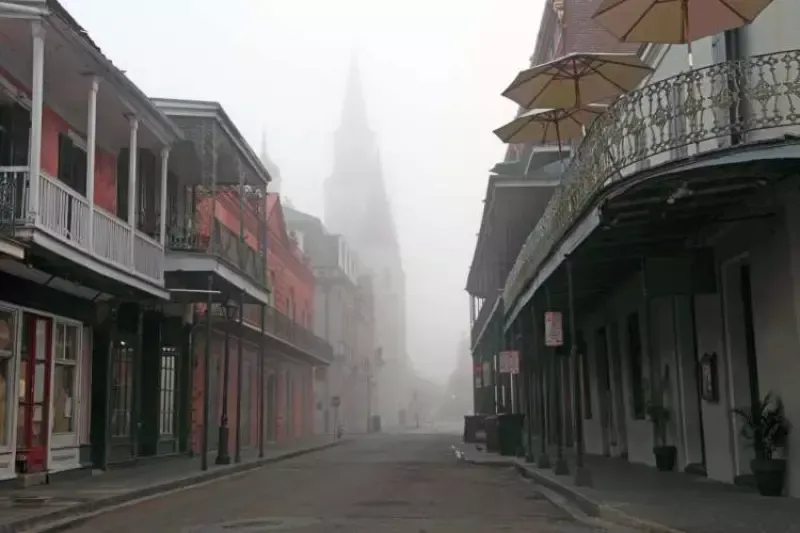 A foggy street with a church in the background and umbrellas on the sidewalk.