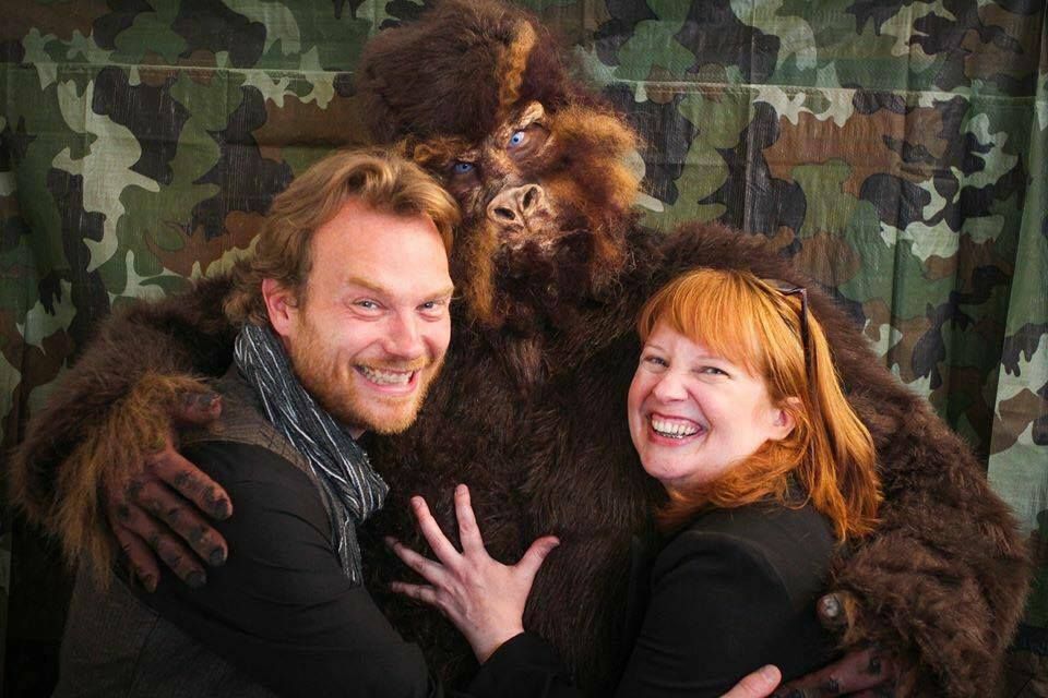 A man and a woman are posing for a picture with a stuffed gorilla.