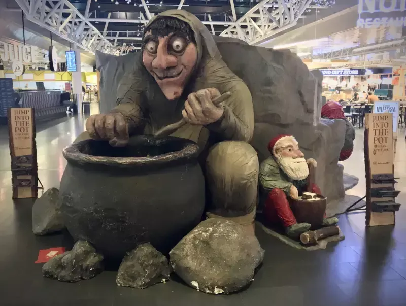 A statue of a troll stirring a pot next to a statue of santa claus.