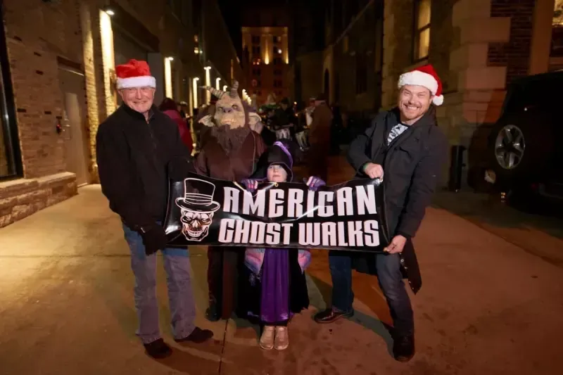 A group of people standing on a sidewalk holding a sign that says american ghost walks.