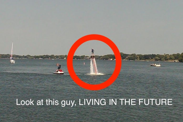 A man is flying through the air on a jet ski with the words look at this guy living in the future below him