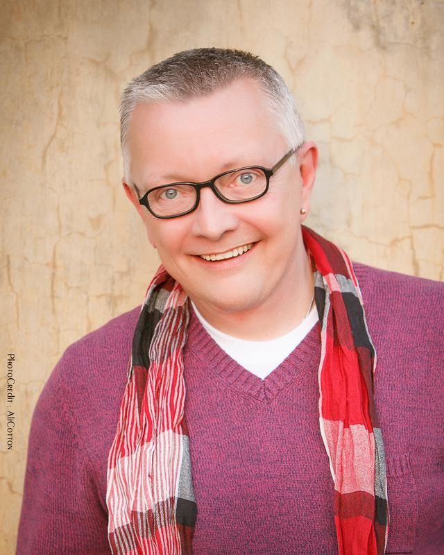 A man wearing glasses and a scarf smiles for the camera