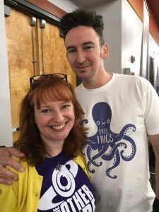 A man and a woman are posing for a picture . the woman is wearing a purple shirt with an octopus on it.